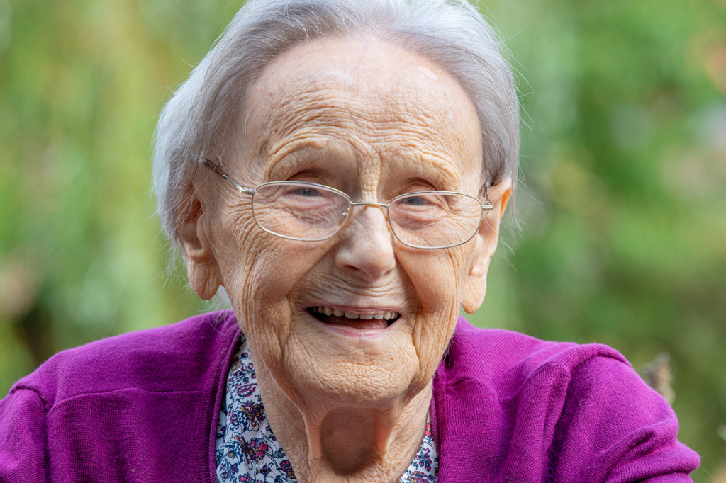 Eine Frau,  über 90 Jahre alt, mit Brille, freut sich und lacht.